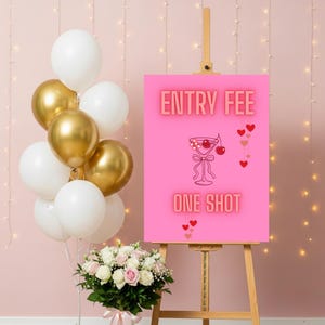 以下が含まれることがあります： イーゼルに立てられたピンク色の看板。光るフォントで「ENTRY FEE」と「ONE SHOT」の文字。カクテルグラスのイラストが中央にあります。白と金の風船と花のブーケが左側にあります。