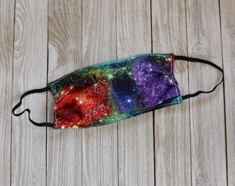 May include: A face mask with a colorful galaxy print. The mask is made of fabric and has a black elastic band.