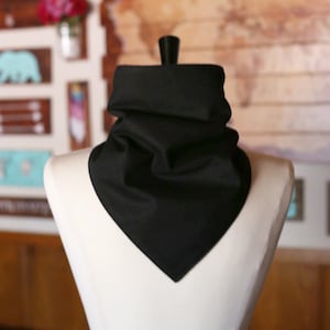 May include: A black fabric neck scarf with a pointed end. The scarf is folded and draped over a white mannequin.