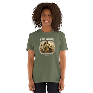 May include: Olive green t-shirt featuring the text "SHE AROSE" above an illustration of a woman warrior holding a spear. The illustration is in sepia tones, with the text "A Judge of Israel" below.