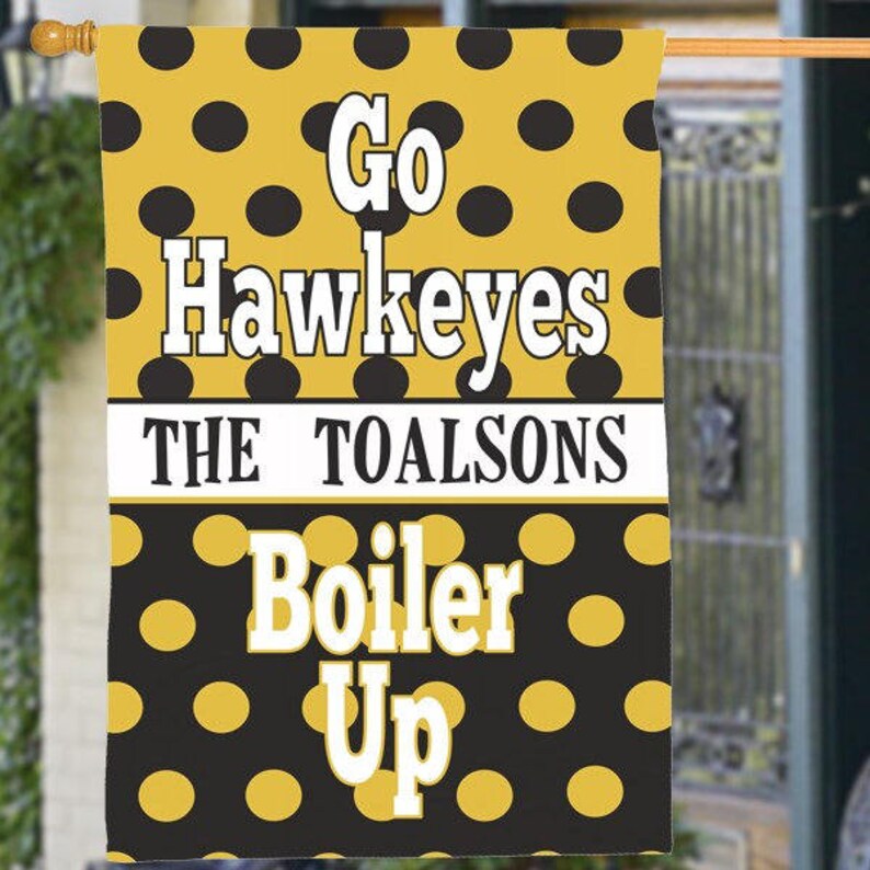 May include: A decorative outdoor flag with a yellow and black polka dot pattern. The flag features the words "Go Hawkeyes" and "Boiler Up" in white block letters. The name "The Toalsons" is also displayed.