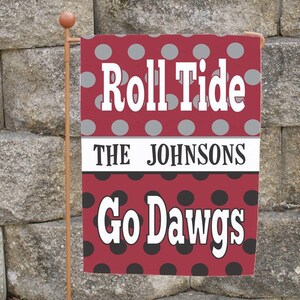 May include: A burgundy garden flag with white text that reads "Roll Tide" and "Go Dawgs". The flag has a polka dot pattern in gray and black. The text "The Johnsons" is in a white banner.