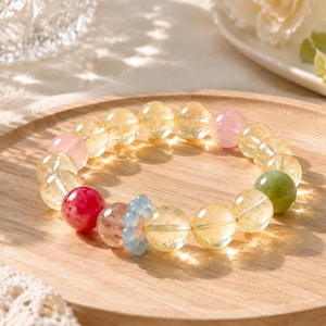 Puede incluir: Una pulsera de cuentas con esferas de citrino amarillo translúcido, intercaladas con una cuenta verde opaca, una cuenta roja brillante, una cuenta rosa pálido, una cuenta color melocotón moteada y una pequeña cuenta espaciadora azul claro en forma de flor.