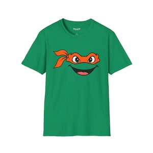 Peut inclure: Un t-shirt vert vif à manches courtes avec une impression graphique représentant un visage de personnage de dessin animé portant un masque orange. Le personnage a de grands yeux et une large bouche souriante. Col rond et coupe standard.