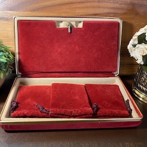 May include: Open red velvet jewelry box with three matching pouches. The box has a gold trim and a latch closure. The interior is lined with a cream-colored material.