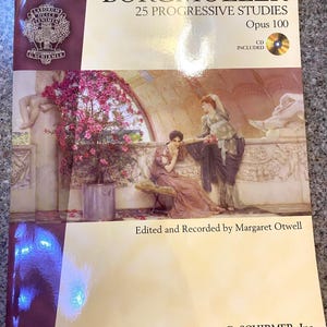 May include: A music book titled "Burgmüller 25 Progressive Studies Opus 100" by G. Schirmer, Inc. The cover features a classical painting of women in flowing gowns, with a CD included. The book is part of the Hal Leonard Piano Library.