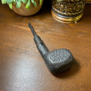 May include: A black tobacco pipe with a textured, rugged bowl and a smooth, slender stem. The pipe features a dark, matte finish across its entire surface, showcasing a distinct contrast between the rough, pitted texture of the bowl and the sleek, tapered mouthpiece.