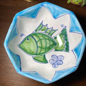 Może przedstawiać: Ręcznie malowana ceramiczna miska z białym wnętrzem i niebieską obwódką. Miska ma zielony wzór ryby i niebieski kwiat. Kształt miski to nieregularny ośmiokąt.