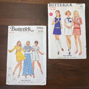 May include: A set of three ceramic mugs with a speckled, cream-colored glaze. Each mug features a different hand-painted design: a blue and green leaf, a yellow flower, and a red berry. The mugs have a simple, rounded shape.