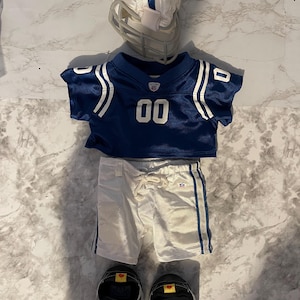 May include: A miniature football uniform set including a white helmet with a blue stripe, a blue jersey with the number 00 and white shoulder stripes, white shorts with blue side stripes and a drawstring, and a pair of black athletic shoes.