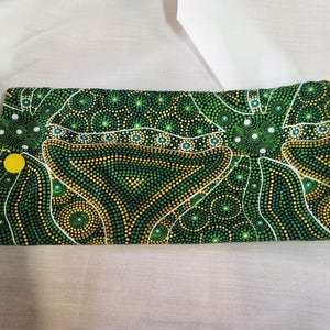 Puede incluir: Un artículo rectangular de tela doblada con un vibrante estampado de puntos verdes, amarillos y blancos. El diseño presenta formas orgánicas y un cierre de botón amarillo. El artículo es probablemente una funda o una bolsa.