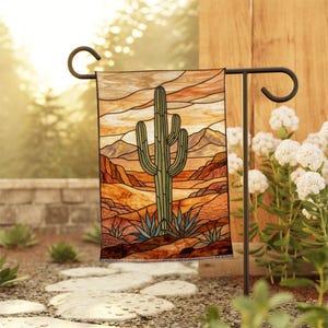 Peut inclure: Un drapeau de jardin rectangulaire présentant une illustration style vitrail d'un grand cactus saguaro vert dans un paysage désertique avec des montagnes orange et brunes sous un ciel de coucher de soleil chaud, suspendu à un support en métal noir.