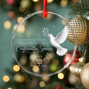May include: A clear, circular glass ornament with a faceted edge, hanging from a red ribbon. It features a white dove illustration, small stars, and the text: WITH HEARTFELT THANKS FOR GUIDING ME AS MY Confirmation Sponsor LOVE, EMILY MAY 18, 2026.