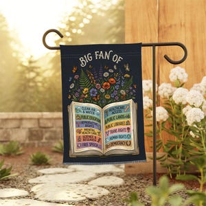 May include: A dark blue garden flag featuring an open book illustration with colorful flowers above it. The text reads BIG FAN OF followed by a list of social causes including Clean Air & Water, Public Education, Healthcare Access, and Democracy.