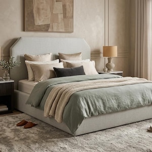 May include: A light gray upholstered bed with a sage green duvet and a cream-colored knitted throw. The bed is adorned with several pillows in neutral tones. Two bedside tables with lamps flank the bed, and a rug covers the floor.