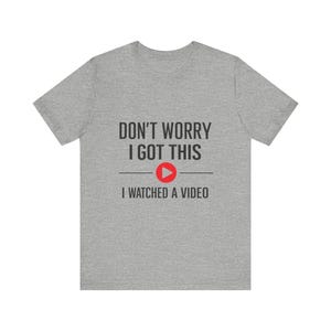 May include: A heather gray t-shirt with the text "DON'T WORRY I GOT THIS" above a red play button icon and the text "I WATCHED A VIDEO". The shirt is a casual wear item.