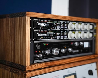 May include: Two black Distressor audio compressor units stacked above a black dbx 165A compressor limiter unit, all housed within a custom-built wooden rack enclosure featuring a dark brown wood grain finish and visible horizontal wood layering.