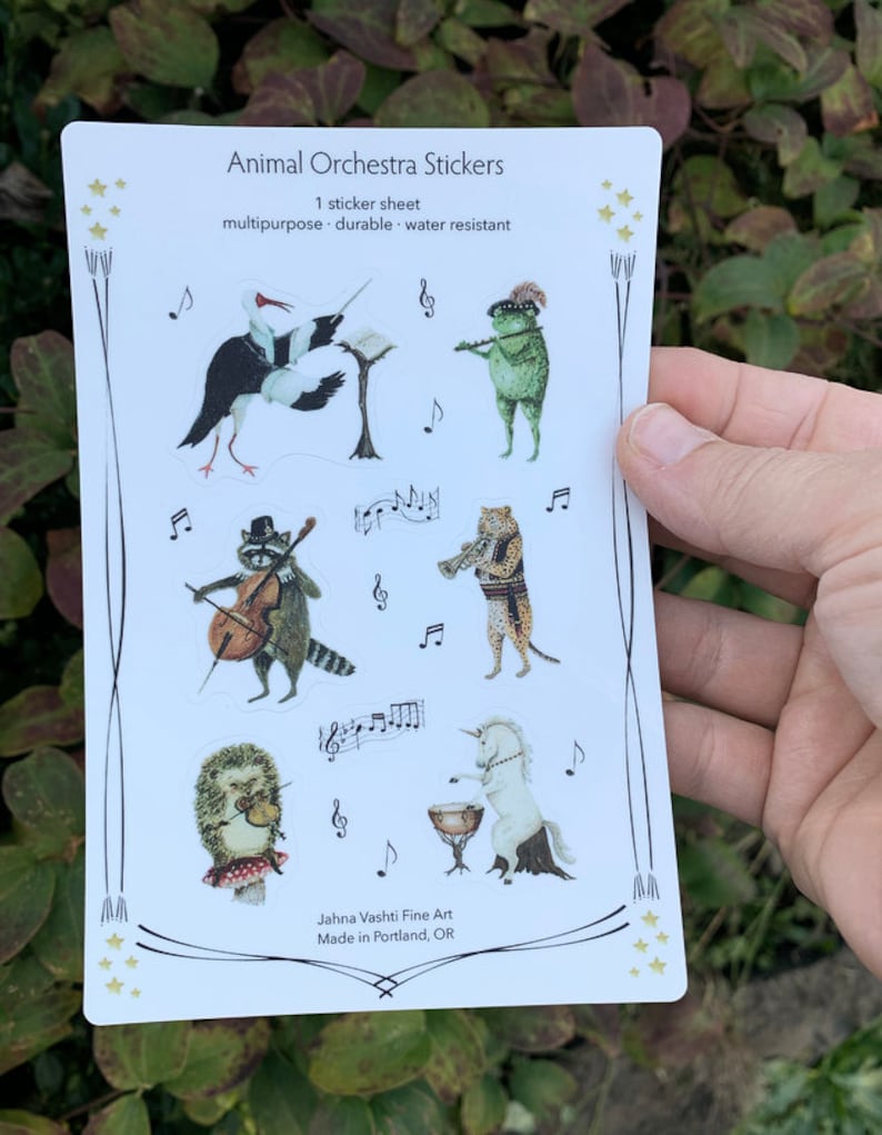 May include: A sheet of stickers featuring an animal orchestra. The stickers are colorful and feature a variety of animals playing musical instruments. The text on the sheet reads "Animal Orchestra Stickers" and "1 sticker sheet, multipurpose, durable, water resistant".