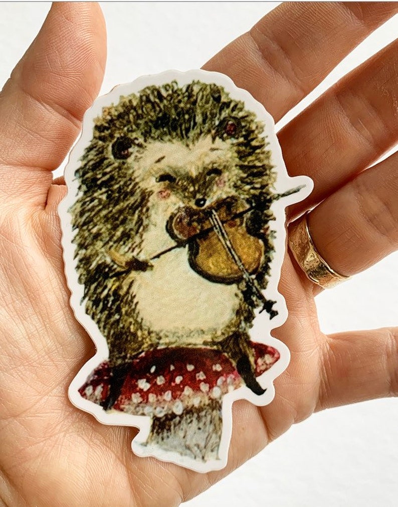May include: A sticker featuring a cartoon hedgehog playing a violin while sitting on a red and white polka dot mushroom.