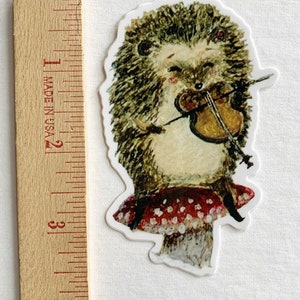 May include: A sticker of a hedgehog playing a violin while sitting on a red mushroom with white polka dots.
