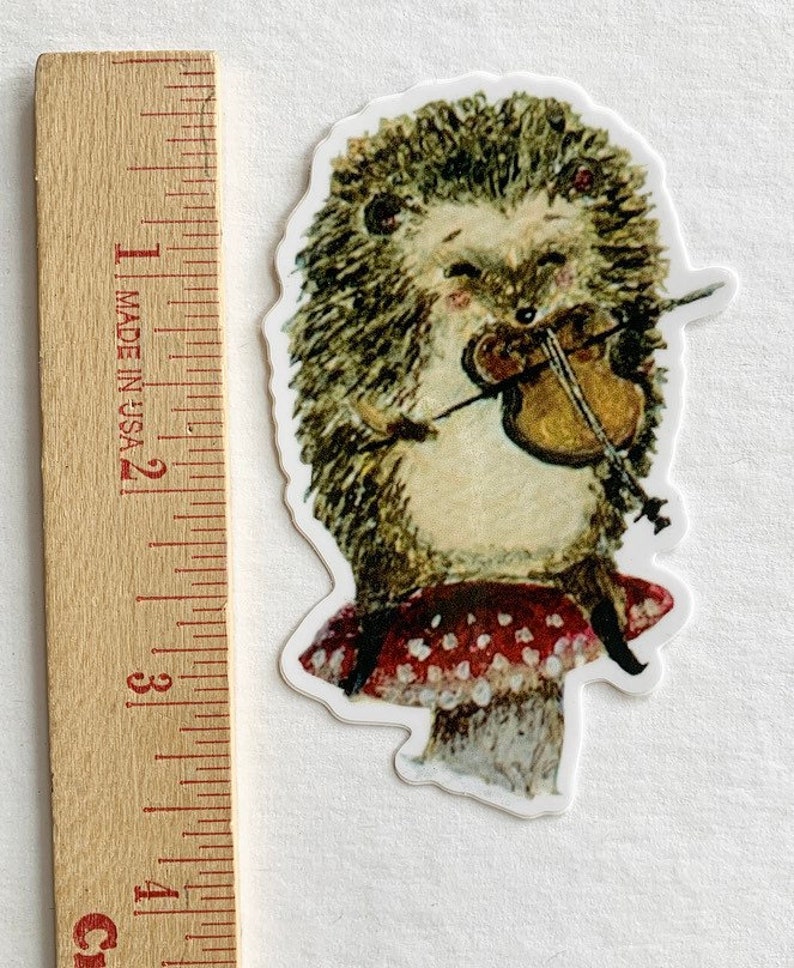 May include: A sticker of a hedgehog playing a violin while sitting on a red mushroom with white polka dots.