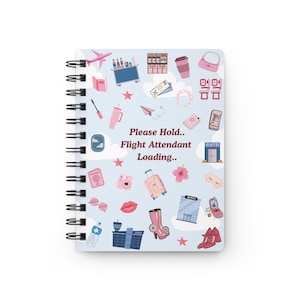 Puede incluir: Un cuaderno con espiral con una cubierta azul claro con ilustraciones de temática de viajes. La cubierta incluye un avión rosa, equipaje y el texto "Please Hold.. Flight Attendant Loading.."