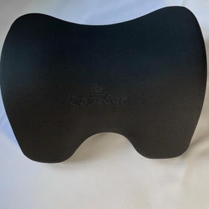 Pode incluir: Um apoio de cabe&ccedil;a preto para carro com formato contornado para suporte do pesco&ccedil;o. O apoio de cabe&ccedil;a tem um acabamento liso e fosco e apresenta o texto bordado "CozeCar" em um tom de preto mais claro.