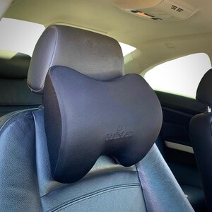 Pode incluir: Uma almofada preta para encosto de cabe&ccedil;a de carro com o nome da marca "CozeCar" impresso. A almofada est&aacute; presa a um assento de carro preto. O encosto de cabe&ccedil;a tem uma forma curva, projetada para conforto e suporte.