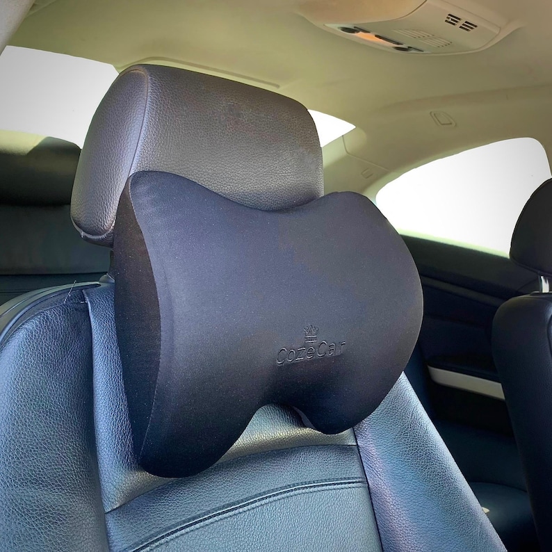 Pode incluir: Uma almofada preta para encosto de cabe&ccedil;a de carro com o nome da marca "CozeCar" impresso. A almofada est&aacute; presa a um assento de carro preto. O encosto de cabe&ccedil;a tem uma forma curva, projetada para conforto e suporte.