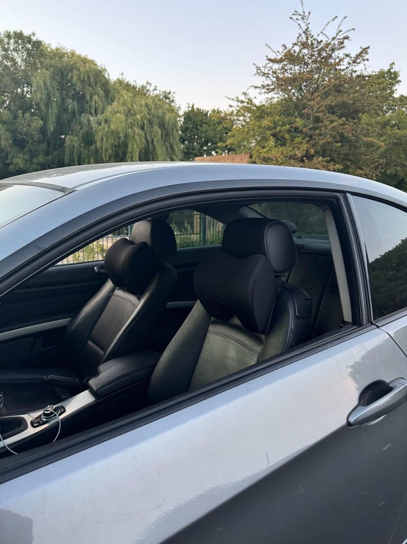 Pode incluir: Um carro coup&eacute; prateado com interior em couro preto. Os bancos dianteiros s&atilde;o vis&iacute;veis, com encostos de cabe&ccedil;a e apoios de bra&ccedil;os. O carro est&aacute; estacionado ao ar livre com &aacute;rvores ao fundo.
