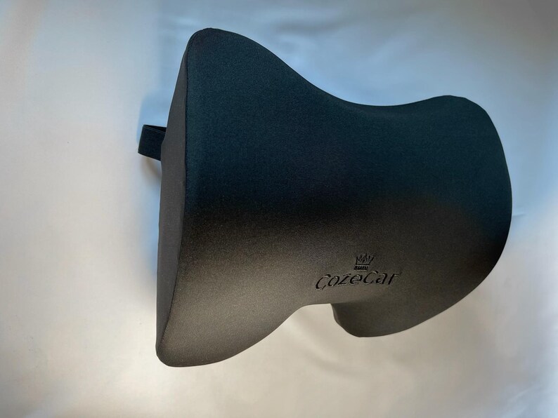 Pode incluir: Uma almofada de apoio lombar preta com o nome da marca "CozeCar" impresso na frente. A almofada tem um design curvo e uma al&ccedil;a na lateral. A almofada foi projetada para fornecer suporte para a regi&atilde;o lombar.