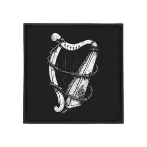 May include: Black square patch featuring a detailed white illustration of a harp wrapped in barbed wire. The harp has a Celtic knot design at the base. The patch has a black border.