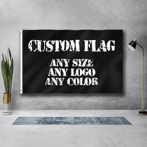 May include: A black custom flag with white text that reads "CUSTOM FLAG, ANY SIZE, ANY LOGO, ANY COLOUR." The flag is hanging on a wall. A plant in a gold pot is to the left of the flag.