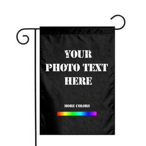 May include: Black garden flag with the text "YOUR PHOTO TEXT HERE" in white, block letters. The bottom of the flag has a rainbow-colored stripe and the words "MORE COLORS". The flag is hanging from a black metal stand.