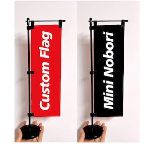 May include: Two mini flags on black stands. One flag is red with the text "Custom Flag" in white. The other flag is black with the text "Mini Nobori" in white. The flags are displayed against a white background.