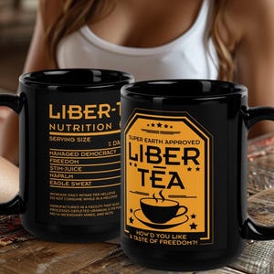 May include: Two black ceramic mugs with yellow text. One mug reads "LIBER-1 NUTRITION" with a list of ingredients. The other mug reads "LIBER TEA" with a teacup graphic and the phrase "How'd you like a taste of freedom?!"