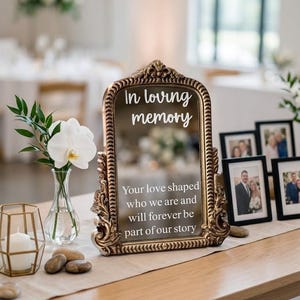 May include: An ornate, antique-style gold mirror with a decorative frame featuring the white text: In loving memory, Your love shaped who we are and will forever be part of our story. The mirror is displayed on a table alongside framed photographs.
