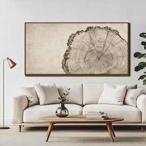 May include: A sepia-toned framed print of a tree cross-section, showcasing concentric growth rings. The artwork is displayed above a cream-colored sofa with matching pillows. A wooden coffee table and a floor lamp with a gold shade are in the foreground.