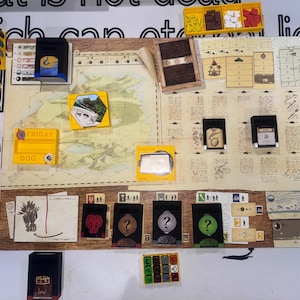 May include: A board game set featuring a large illustrated map board, yellow plastic component trays, black card holders, and various game tokens. The board displays text, icons, and grid sections, with cards labeled Friday, Dog, and other symbols.