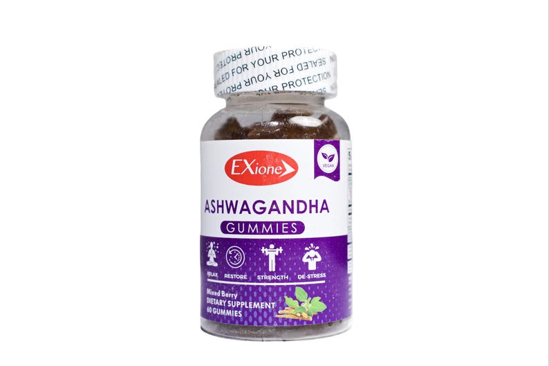 Może przedstawiać: Przezroczysta szklana butelka wypełniona brązowymi żelkami. Etykieta głosi "Exione Ashwagandha Gummies" z fioletowo-białym wzorem. Butelka jest zamknięta białą zakrętką z nadrukiem. Wegański suplement diety.