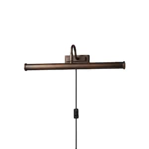 Pode incluir: Uma luz para quadros em bronze escuro com uma longa cúpula cilíndrica horizontal e uma placa de montagem na parede retangular. A luminária possui um braço curvo que liga a cúpula à base e inclui um cabo preto com um interruptor.