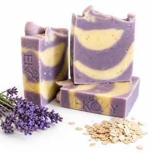 Könnte beinhalten: Vier handgemachte Seifenstücke mit Lavendel- und Haferflocken-Thema. Die Seife hat ein lila-gelbes Wirbeldesign. Ein Zweig Lavendel und ein Haufen Haferflocken liegen neben der Seife. Das Wort "EKOZY" ist auf die Seife gestempelt.