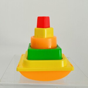 May include: A colorful stacking toy for babies and toddlers. The toy is made of plastic and features four different colored rings that stack on top of each other. The rings are red, yellow, orange, and green. The toy is designed to help children develop their fine motor skills and hand-eye coordination.