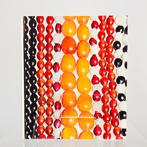 May include: A close-up of a colorful beaded necklace with orange, red, brown, black, and white beads. The beads are arranged in a repeating pattern.