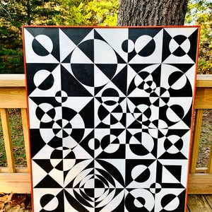 May include: Black and white abstract geometric painting with circles and triangles. The painting is framed in a dark orange wood frame.