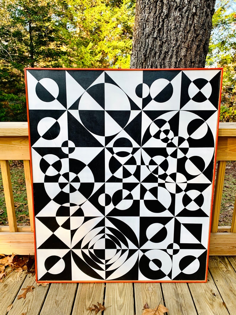 May include: Black and white abstract geometric painting with circles and triangles. The painting is framed in a dark orange wood frame.