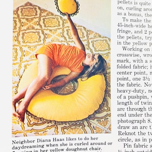 May include: A woman in a bright orange dress is sitting on a large yellow beanbag chair. The beanbag chair has a ruffled edge and is decorated with a pattern of small squares. The woman is holding a yellow pillow with a ruffled edge above her head.