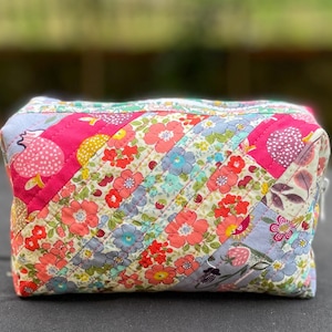 May include: A white ceramic mug with a black handle and the text "But First, Coffee" in a bold, black font. The mug is set against a blurred background, suggesting a cozy setting.