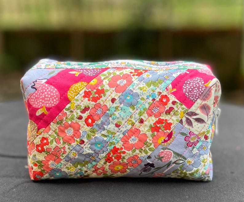 Może przedstawiać: Biały ceramiczny kubek z czarnym uchwytem i napisem "But First, Coffee" pogrubioną czcionką. Kubek jest ustawiony na rozmytym tle, sugerującym przytulne otoczenie.