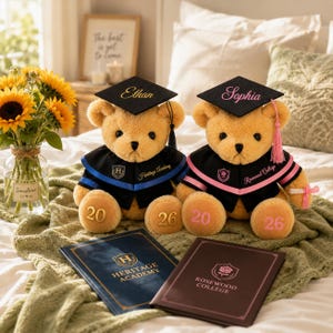 Puede incluir: Dos osos de peluche con gorros y togas de graduaci&oacute;n, cada uno con un nombre en el gorro. Uno tiene detalles en azul, el otro en rosa. Ambos osos tienen los n&uacute;meros 20 y 26 en las patas. Dos libros de graduaci&oacute;n en primer plano.